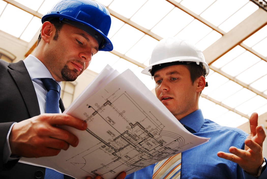 Two architects wearing hard hats reviewing blueprints