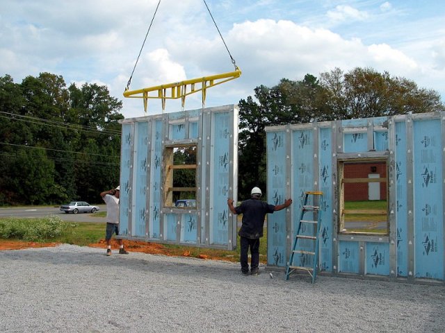 Workers guiding prefabricated wall panel installation
